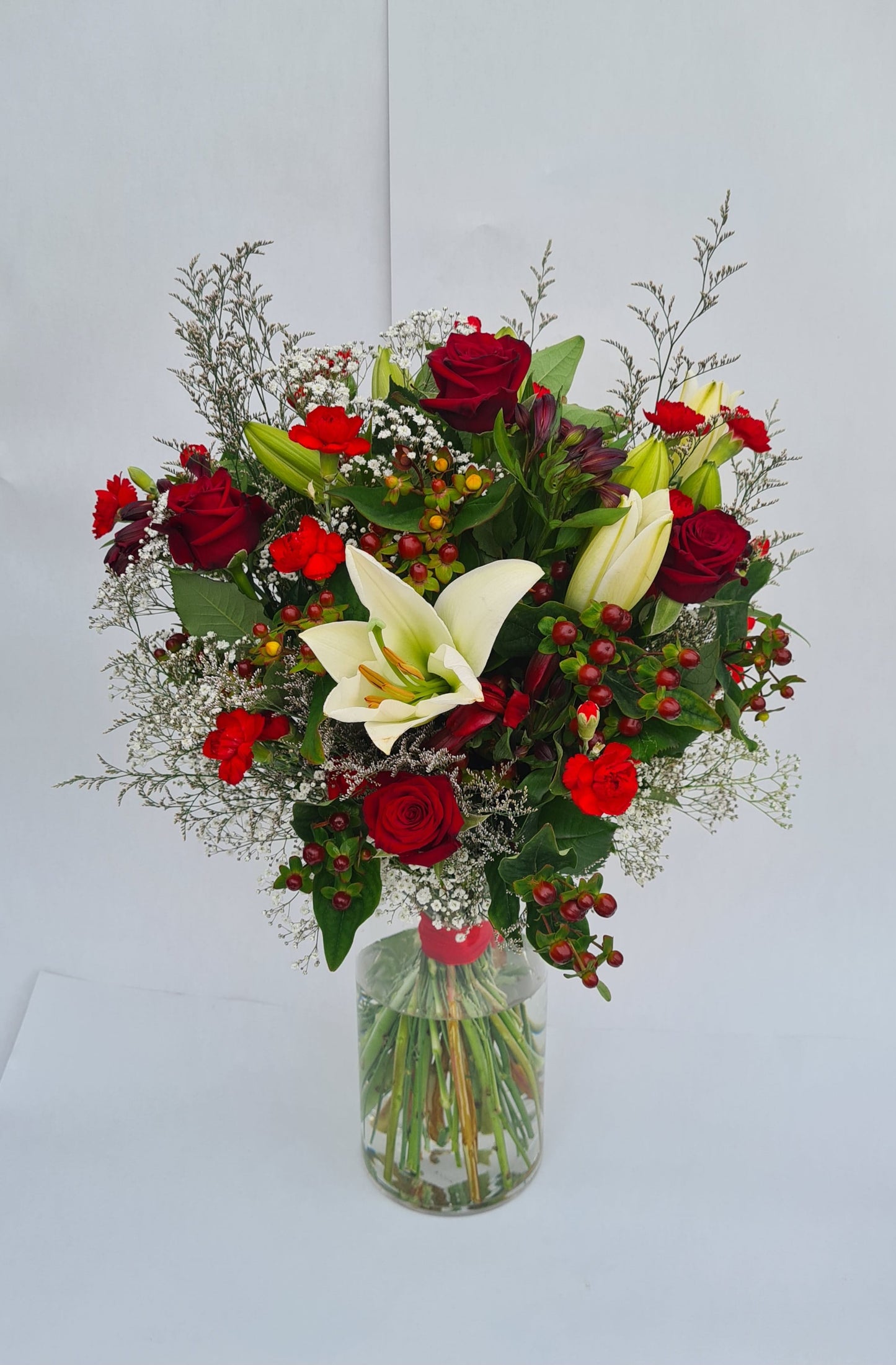 Bouquet of red and white flowers in a clear vase on a light gray background