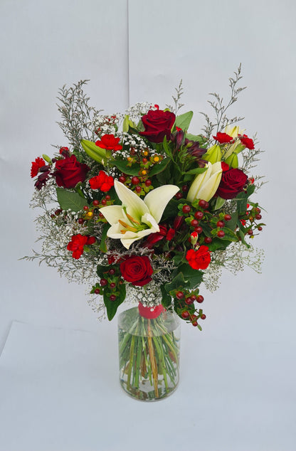 Bouquet of red and white flowers in a clear vase on a light gray background